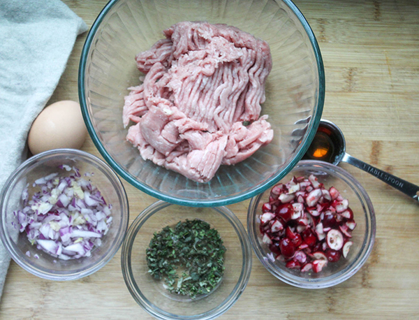 Ground turkey, onions, fresh herbs, cranberries, and syrup on a cutting board