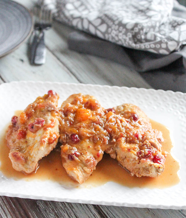 Three boneless chicken breasts on a white platter covered with the cranberry and orange sauce