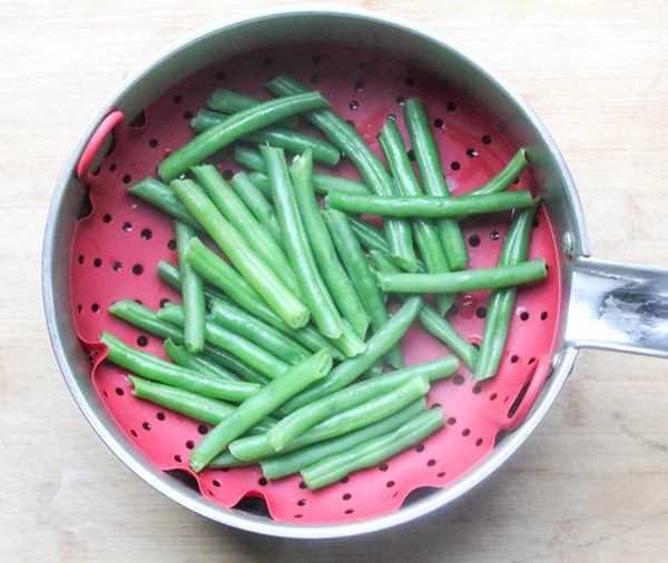 a picture of green beans in a steamer basket in a pan