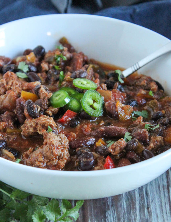 A close up of turkey chili in a bowl with jalapeno slices on top