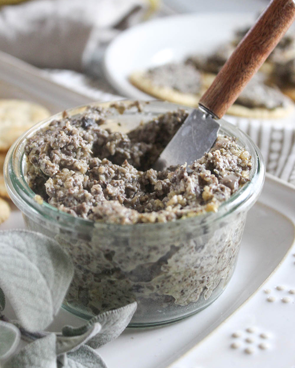 A close up view of vegan mushroom pate in a jar with a spreading knife