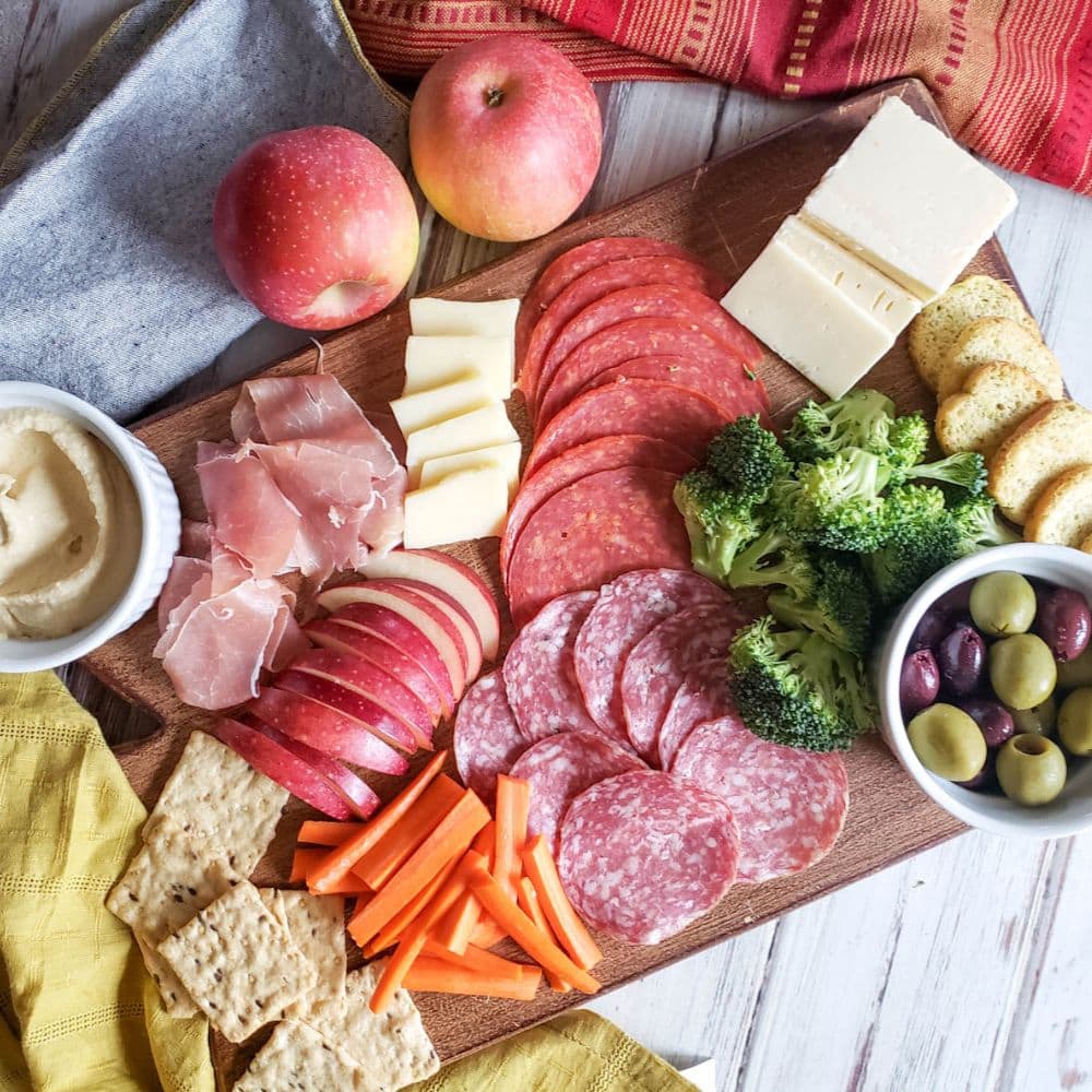 an overhead view of a completed charcuterie board loaded with salami, apples, veggies and cheese