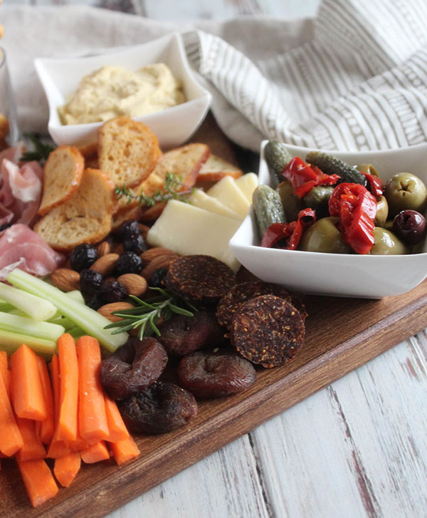 close up of dried apricots, olives, pickles, carrots, almonds and celery on cheese board