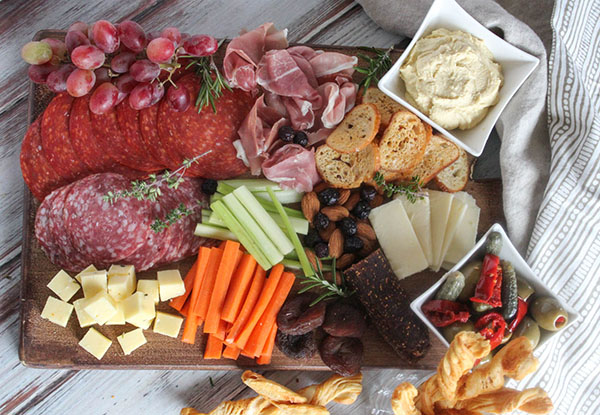 A veiw looking down at a charcuterie board filled with cheese, salami, pepperoni, proscuitto, vegetables and olives