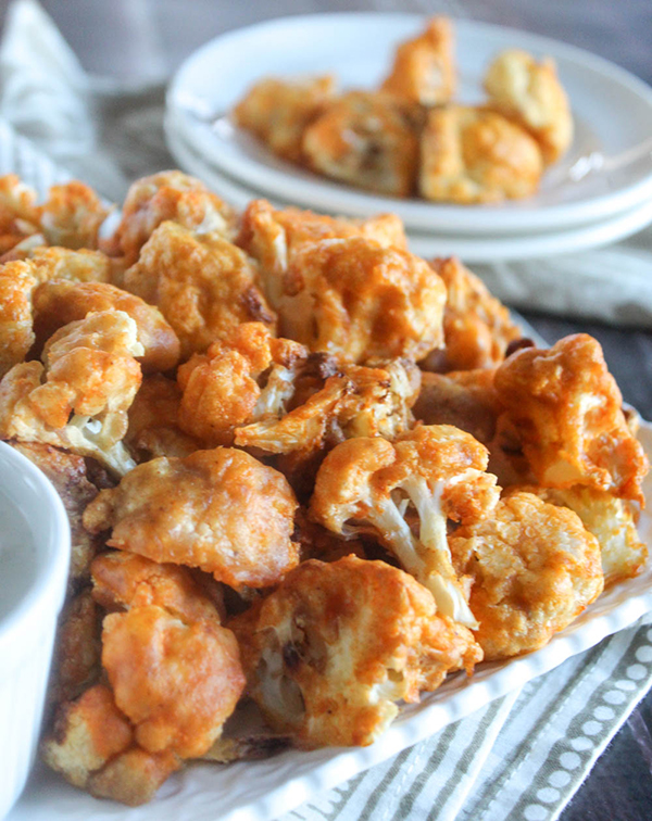 buffalo cauliflower bites on a tray with a serving plate in the background