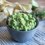 guacamole in a grey bowl with chips in the background