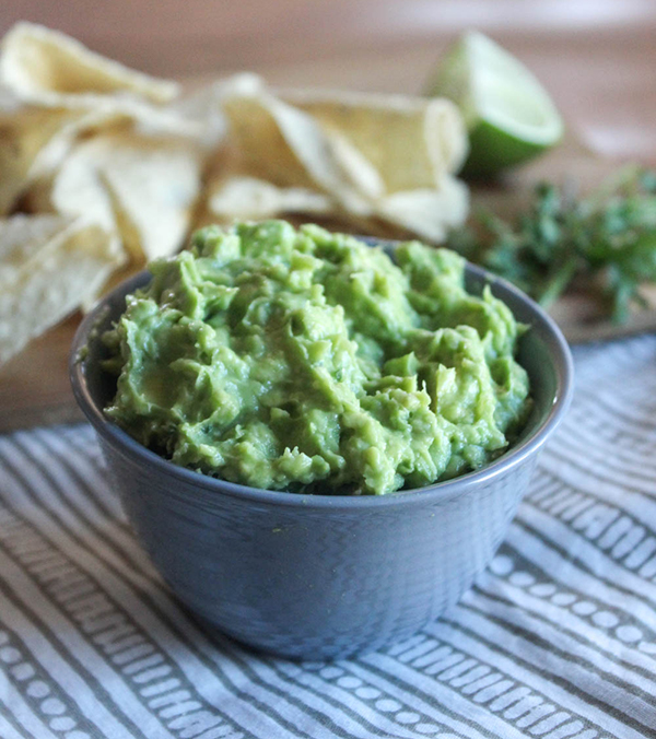 guacamole in a grey bowl with chips in the background