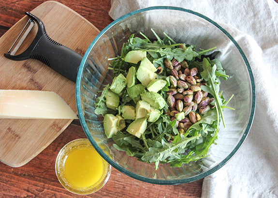 A large salad bowl filled with arugula, avocado and npistachios