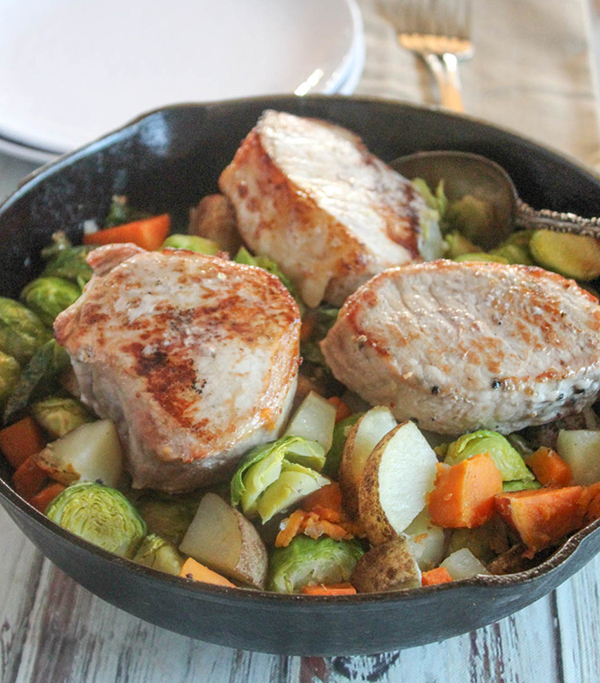 a close up of pork chops with vegetables in a skillet