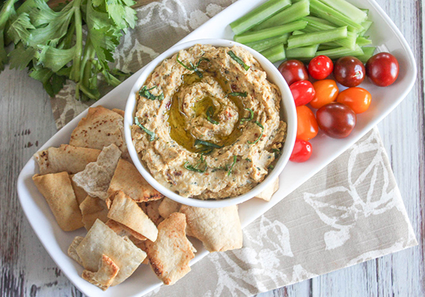 A view looking down at the compted hummus on a plate with chips fresh tomatoes and celery