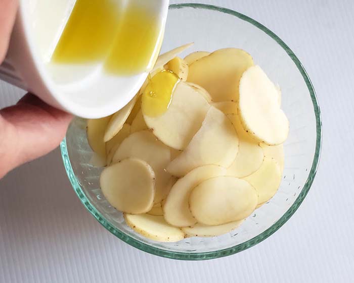 potato slices in a bowl with oil pouring in