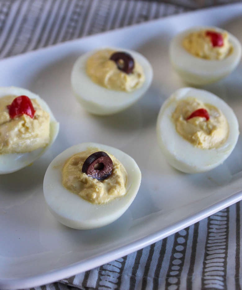 Deviled eggs on a white plate garnished with olives and roasted peppers