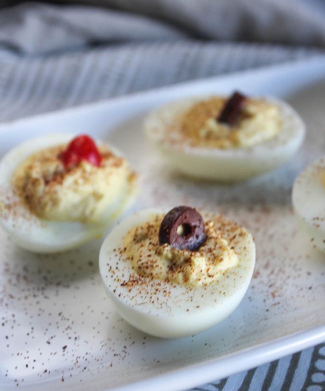 a close up view deviled eggs on a plate garnished with paprika, olives and peppers