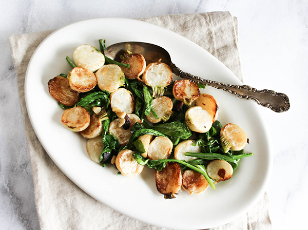 An overhead view of the the turnips, greens with a spoon on a white plate