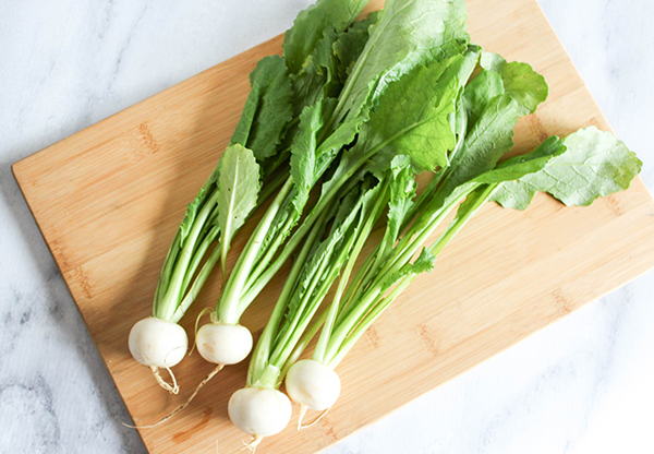 Baby turnips with the greens attached on a cutting board