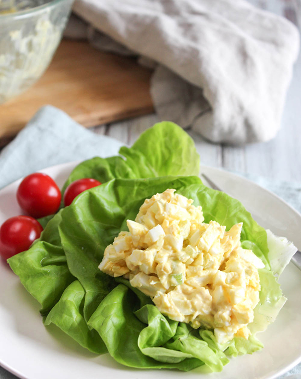 A big scoop of egg salad on lettuce with tomatoes on a white plate