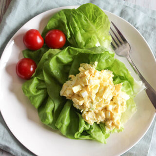 an overhead view of egg salad on a bed of lettuce on a white plate with tomaotes