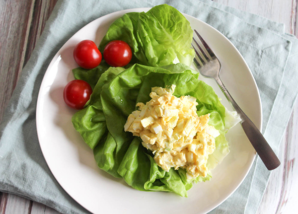 an overhead view of egg salad on a bed of lettuce on a white plate with tomaotes