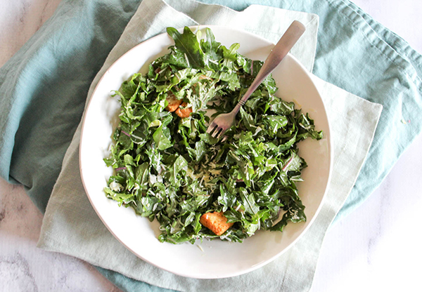 An overhead view of kale caesar salad with a fork