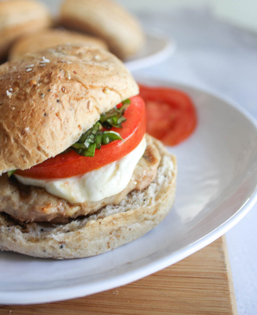 A close up of a chicken burger with cheese melting with a slice tomato on top