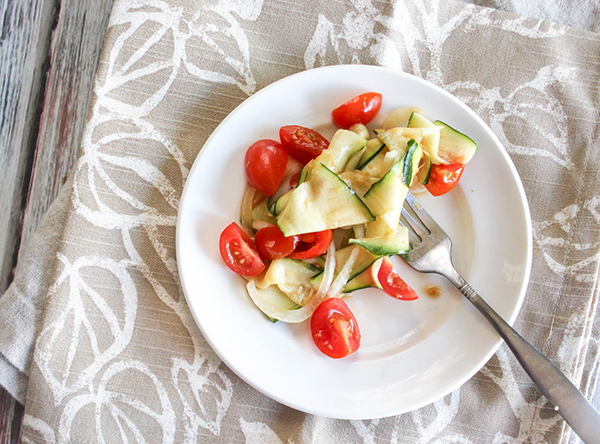 an overhead veiw of zucchini tomatoes and onions in a salad on a plate