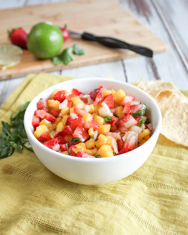 A bowl of fresh mango strawberry salsa with a lime and strawberries in the background