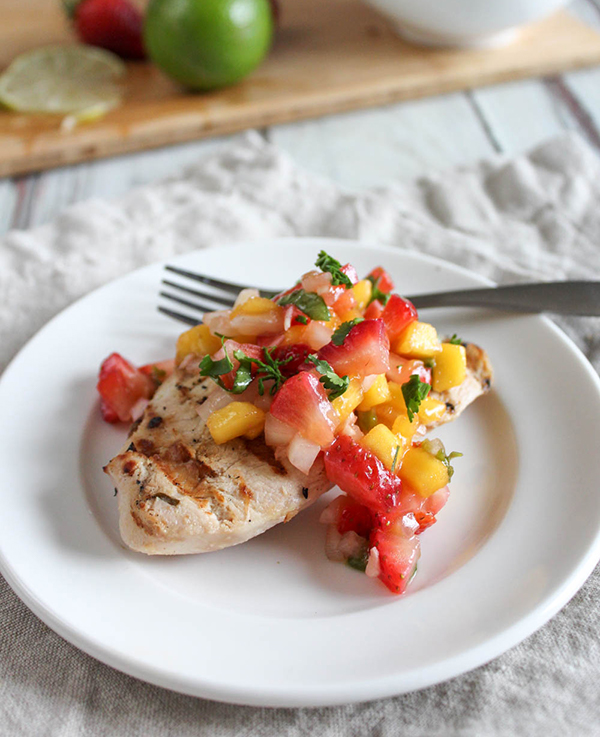 mango salsa on top of grilled chicken on a white plate