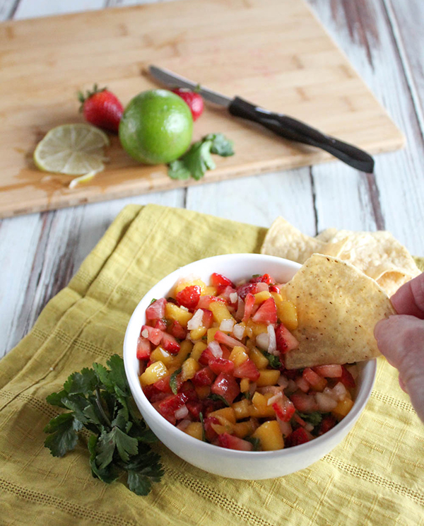 A bowl of salsa with a chip being dipped into it.