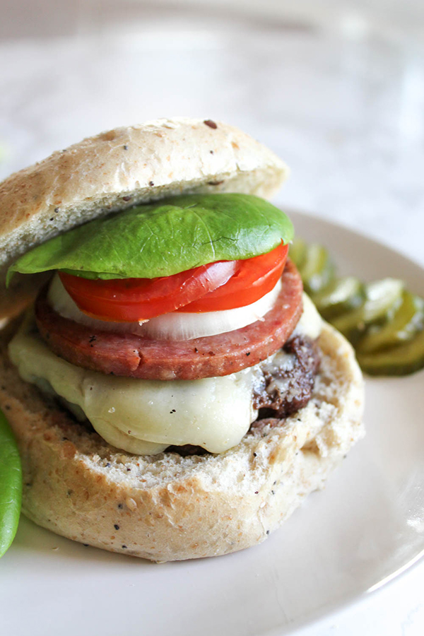 A burger on a roll with melted cheese, tomatoes, lettuce and tomatoes