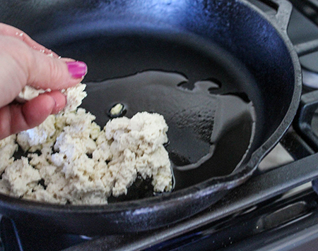 tofu being crumbled by hand into a pan