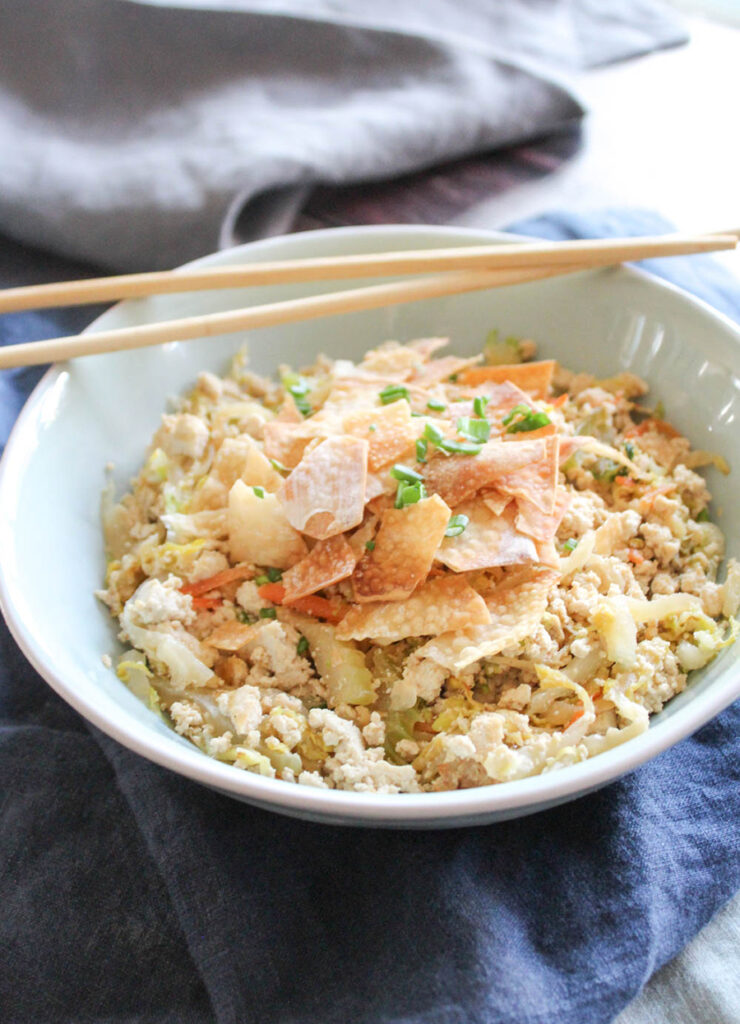 egg roll in a bowl with cripsy baked won ton wrappers on top chop sticks on the side
