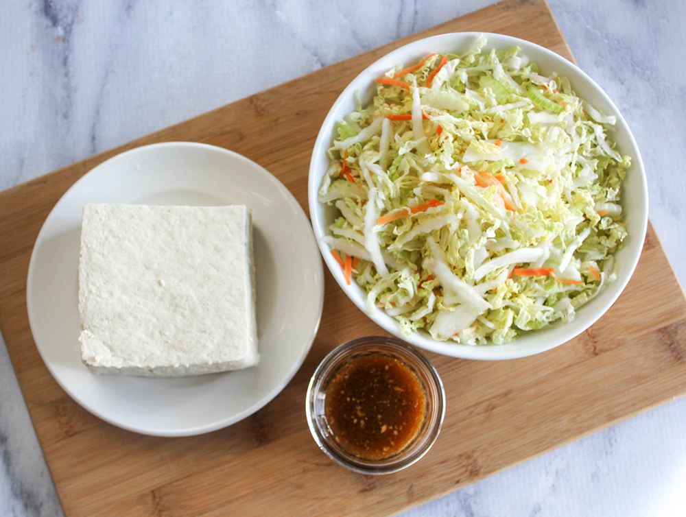 an overhead view of egg roll bowl ingrdients: tofu block, sauce and shredded abbage