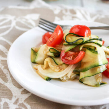 zucchini ribbons with cherry tomatoes on a white plate with a fork