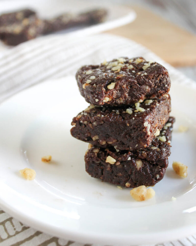 a stack of brownies on a white plate with walnuts sprinkled