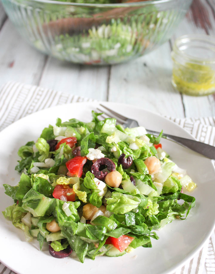 greek chopped salad on a white plate with a fork