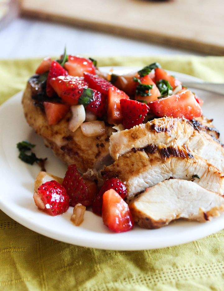 A close up of sliced grilled chicken breast on a plate with strawberry salsa