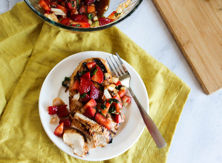 An overhead shot of grilled chicken with strawberries on a plate with a fork