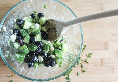 ALL OF THE SALAD INGREDIENTS MIXED TOGETHER IN A GLASS BOWL WITH A WOODEN SPOON