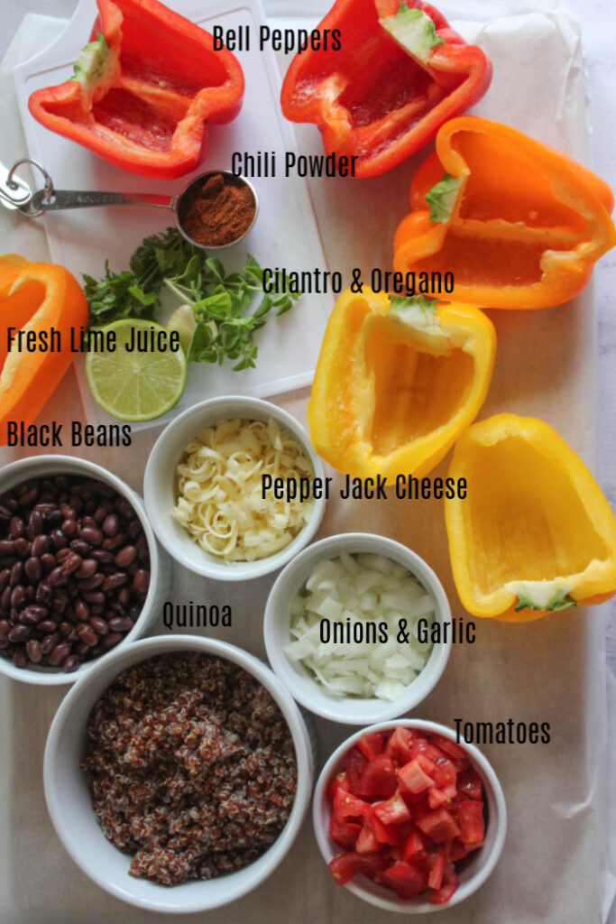 The ingredients on a board, bell peppers, chili powder, cilantro and oregano, lime, shredded cheese, black beans, onions, cooked quinoa and tomatoes