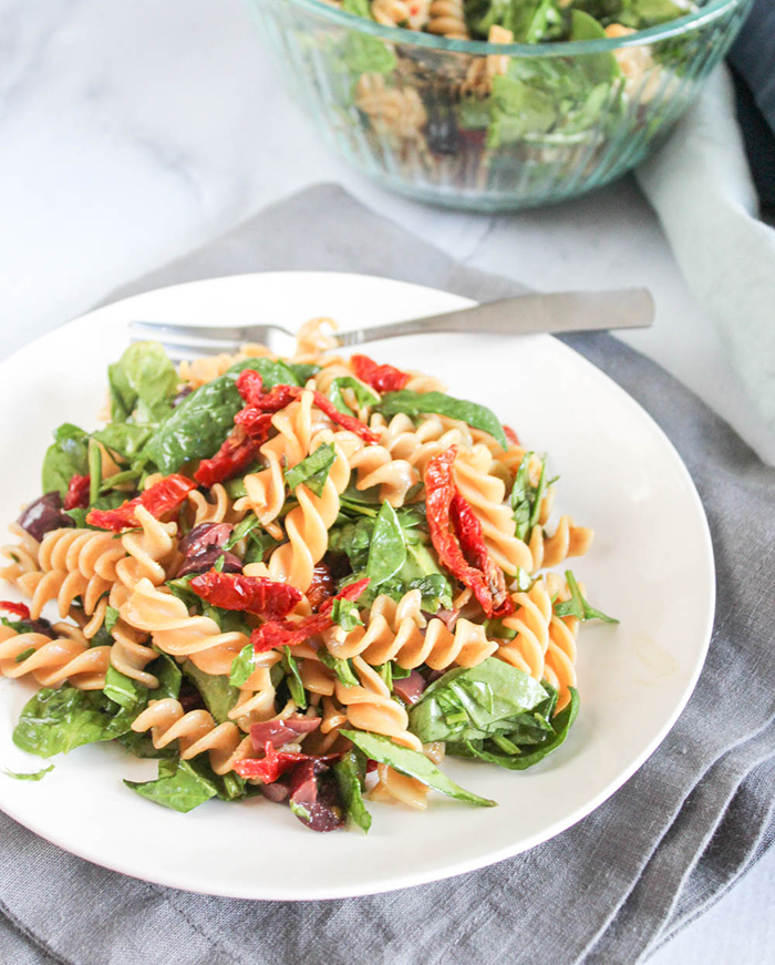 spinach pasta salad on a white plate with a fork