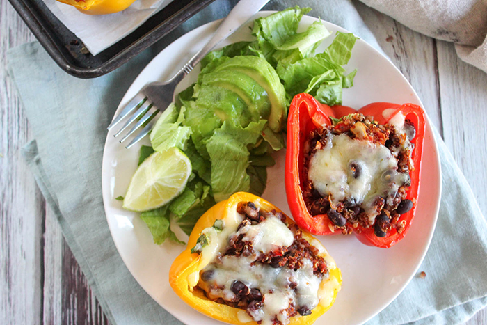 Two stuffed peppers on a plate with a salad and a fork