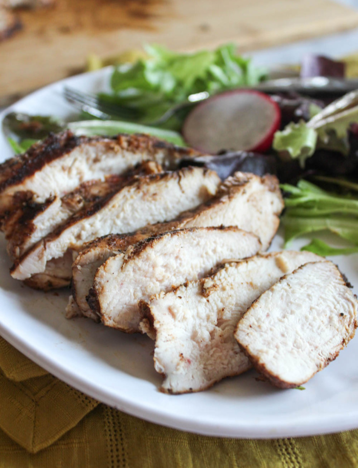 a close up of sliced jerk chicken on a plate with a salad