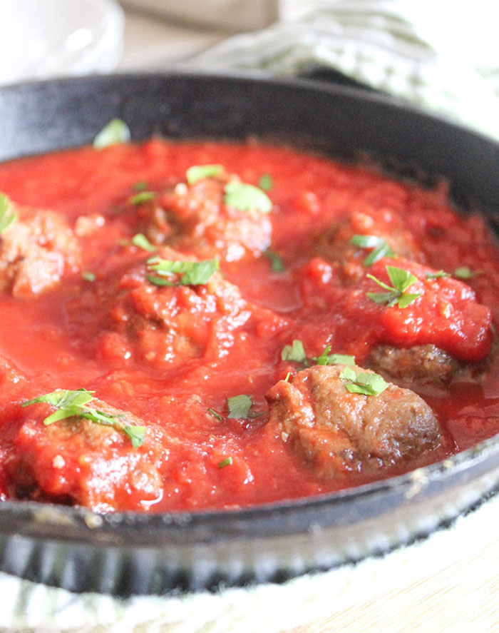 a close up of eggplant meatballs in a pan with red pasta sauce and parsley sprinkled on top