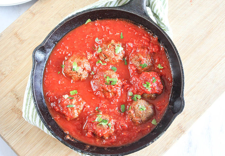 A view looking down at eggplant meatballs in a pan with red pasta sauce and parsley sprinkled on top