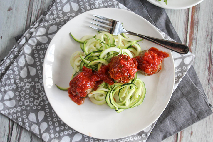 View looking down of eggplant meatballs covered in red sauce on top of zucchini noodles