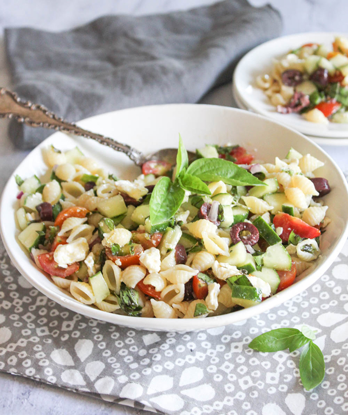 Greek Pasta Salad in a bowl  with a spoon and fresh basil on top