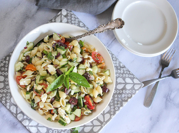 An overhead view of pasta salad in a white bowl with basil on top