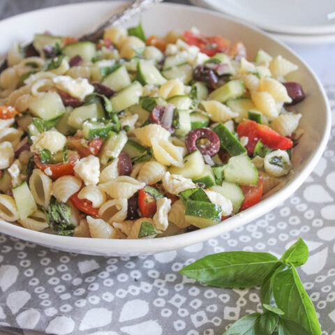 A close up picture of greek pasta salad in a white bowl