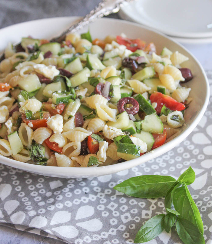 A close up picture of greek pasta salad in a white bowl