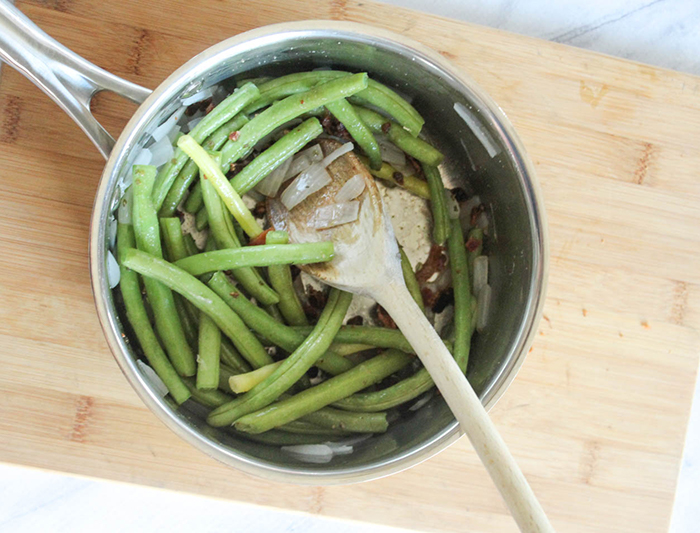 Green beans in a sauce pan with a wooden spoon